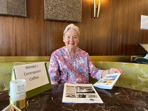 Wendy sitting in Cafe Huguenin in Basel smiling at the camera waiting to welcome new and potential Centrepoint members