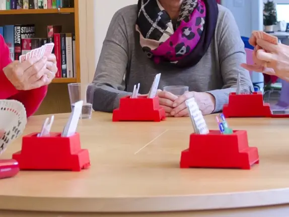 Bridge player hands resting on a desk with red plastic bridge card holders