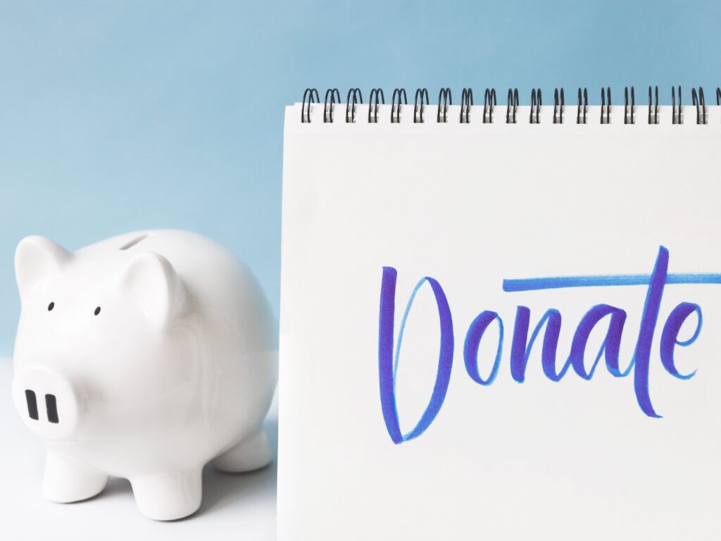 A white piggybank standing next to a sign saying "donate"